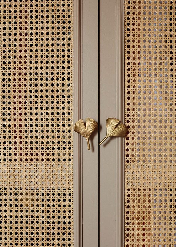 Close view of panelled rattan doors with brass leaf-shaped pulls, used as a material reference.