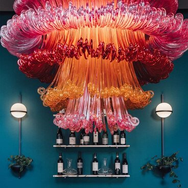 Large pink and orange glass chandelier above a bar, used as a focal-lighting reference.
