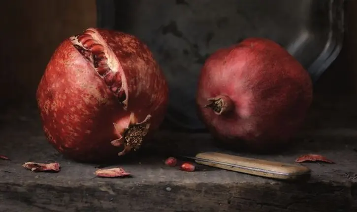 Dark still life with two red pomegranates.